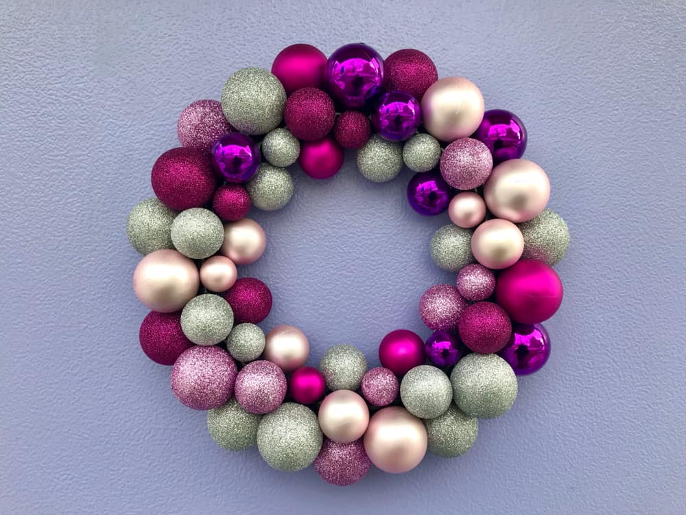 Wreath made from purple, pink, rose gold and mint green baubles of various sizes on a lilac background