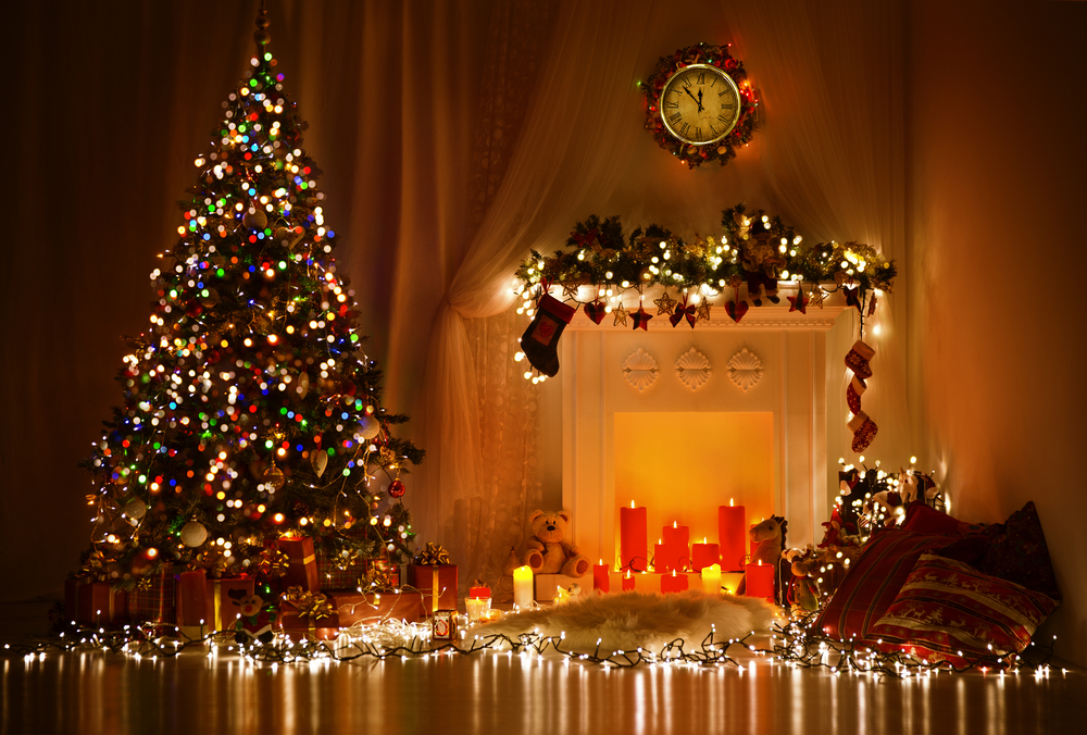 Christmas tree and fireplace with lights, garlands, candles and other decorations in a dimly lit room