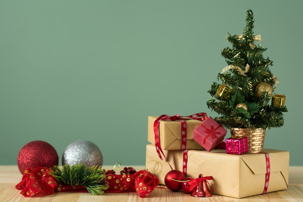 A small Christmas tree and gifts on a wooden table with a green background