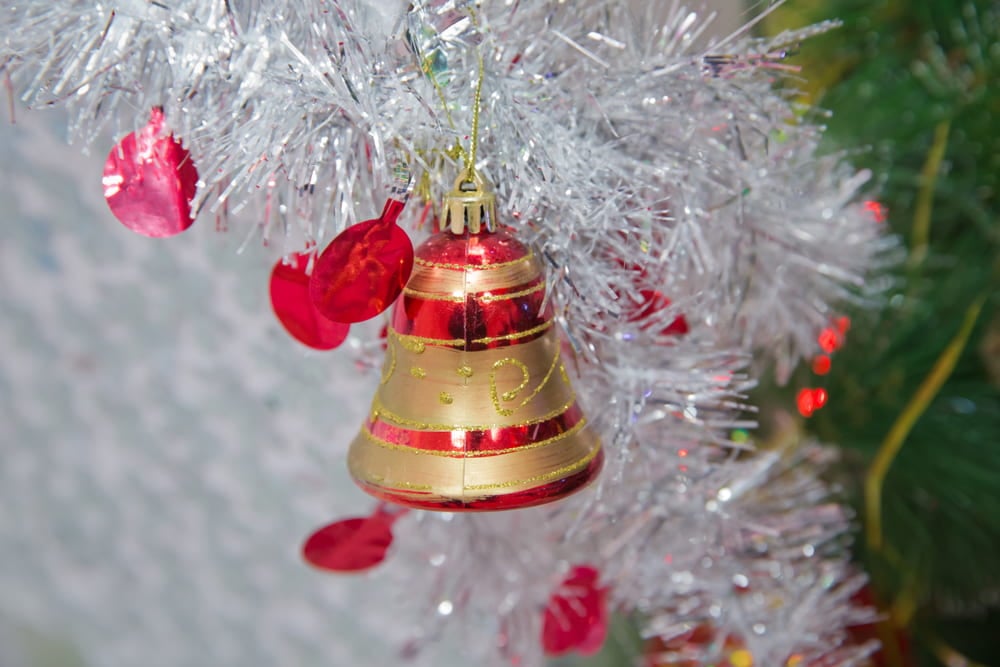 Red and gold jingle bell ornament hanging amongst some silver tinsel