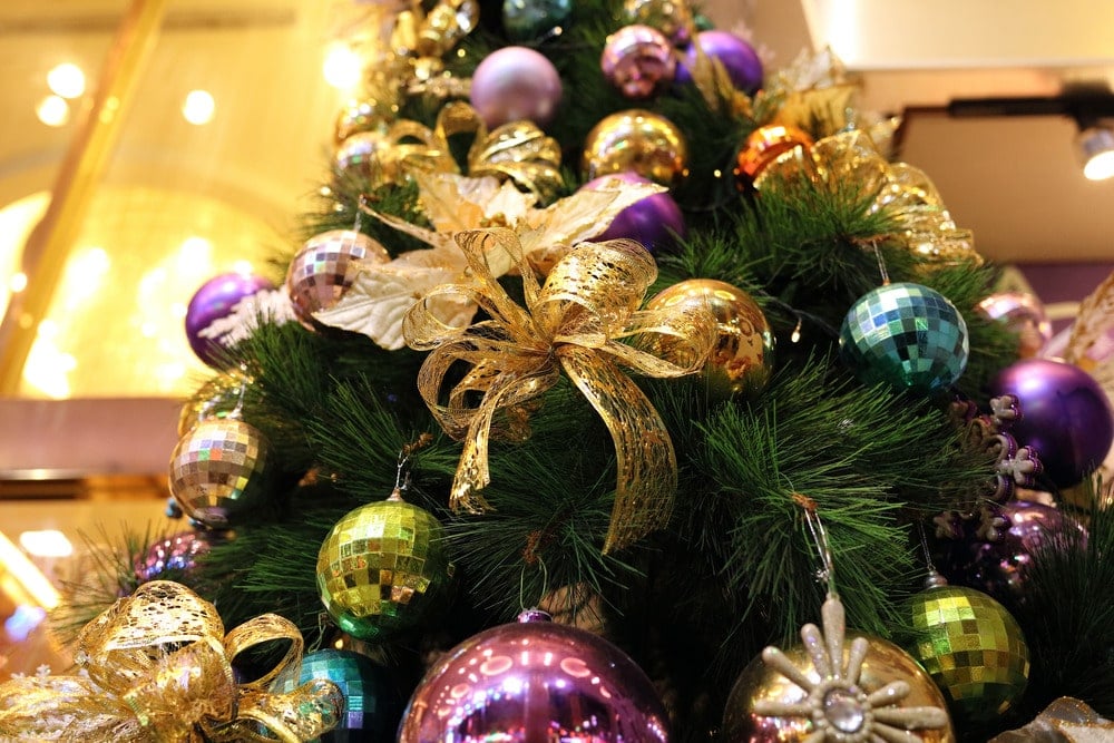 Looking up at a Christmas tree with gold bows and purple, green, gold and blue matte and disco ball baubles