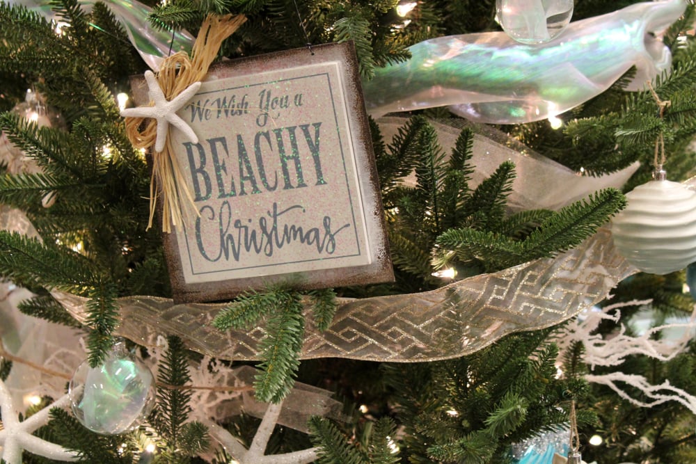 A Christmas tree with starfish ornaments, clear and white bauble, chiffon garland with gold glitter and a sign saying “we wish you a beachy Christmas”