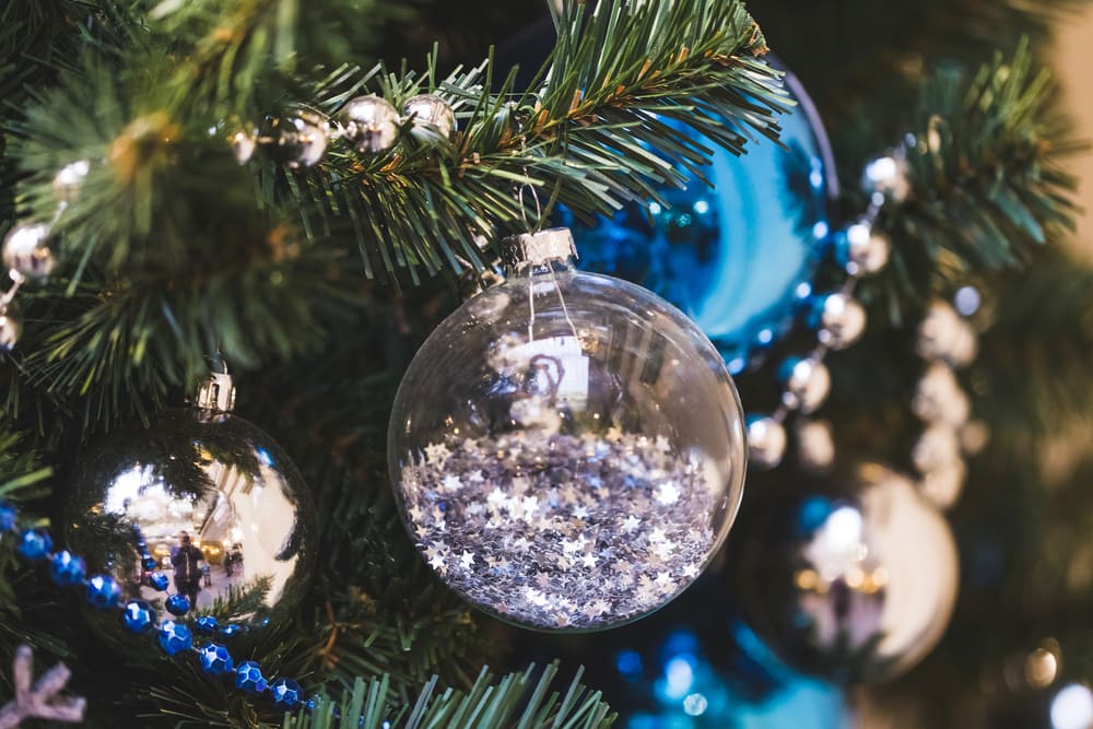 Clear bauble with small tiny stars inside next to a gold bauble and blue beaded garland. In the background are blue and gold baubles with gold beaded garland
