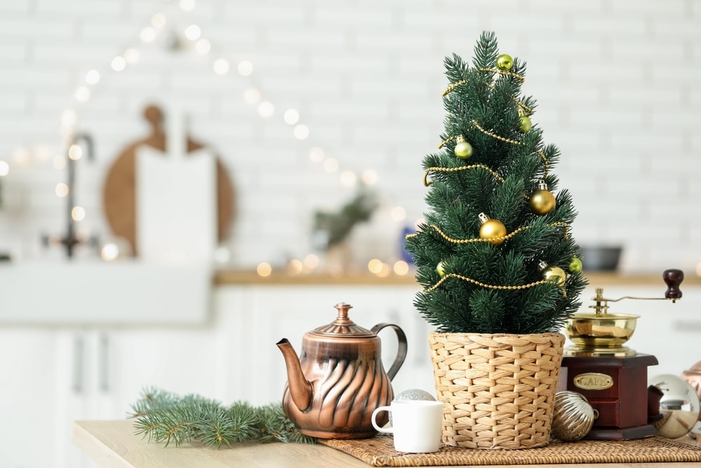 Small tabletop Christmas tree with teapot and coffee grinder on a table in kitchen