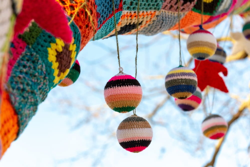 Knitted baubles hanging from a tree with a patchwork covering and a blue sky in the background