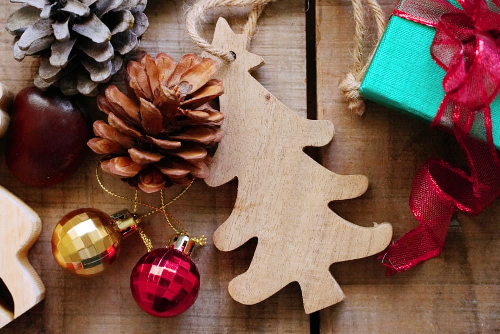 Pine cones, a wooden Christmas tree ornament, tiny baubles and gift box on a wooden background