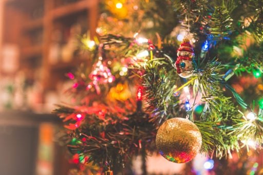 Vibrant and multicoloured Christmas lights wrapped around a classic Christmas tree with other decorations like baubles and a toy Santa.
