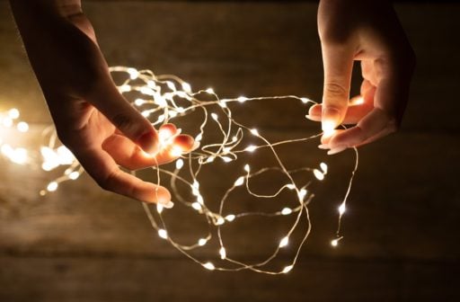 Women’s hands holding a delicate bundle of white string lights in the centre of the image.