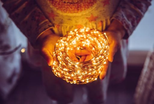 Childrens hands holding a coil of white LED Christmas lights producing a warm circular glow.